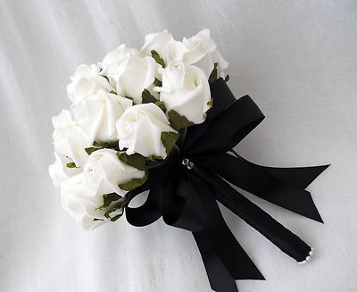 a bouquet of white roses tied to a black ribbon on top of a white sheet