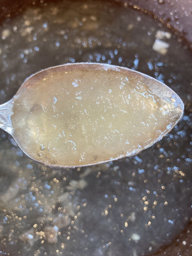 a spoon with some food in it on top of a pan filled with water and oil