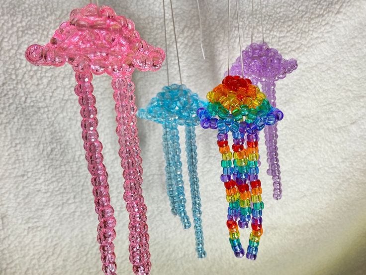 three colorful beaded wind chimes hanging from strings on a white cloth covered wall