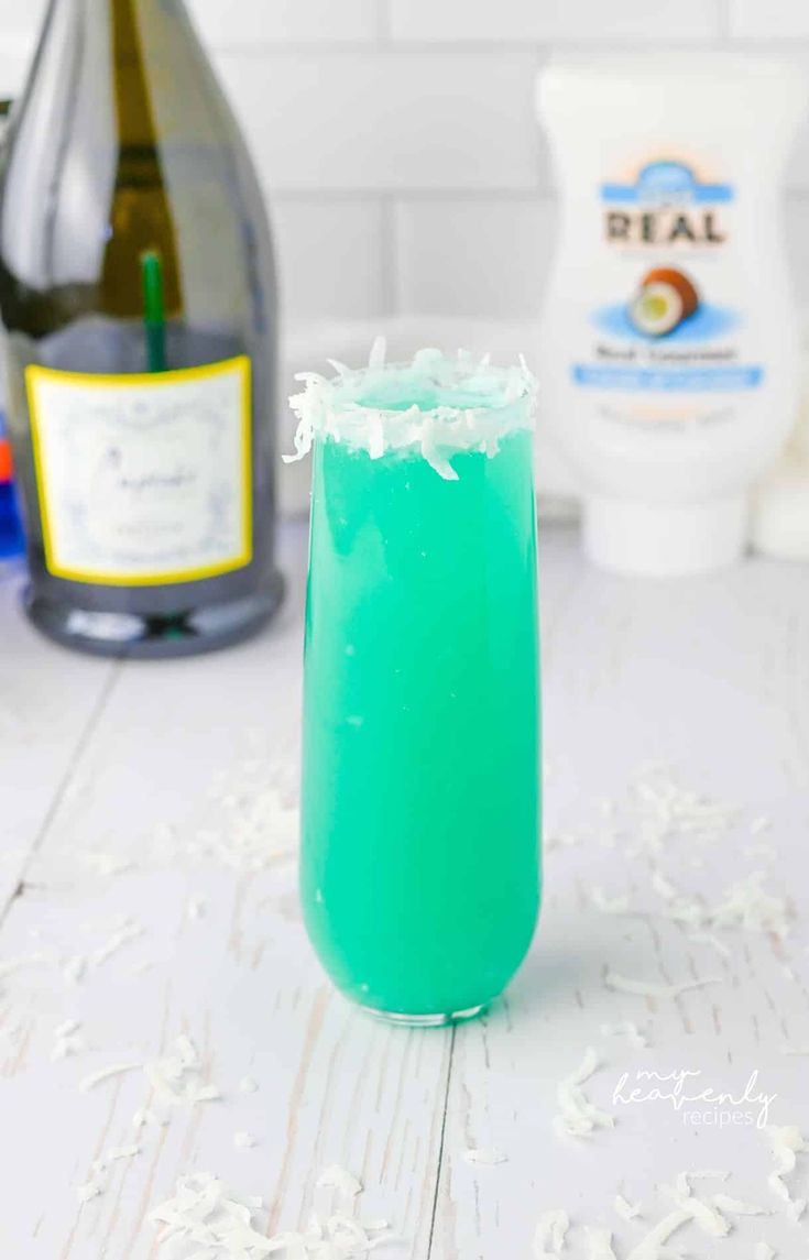 a green drink in a tall glass with coconut flakes on the table next to it