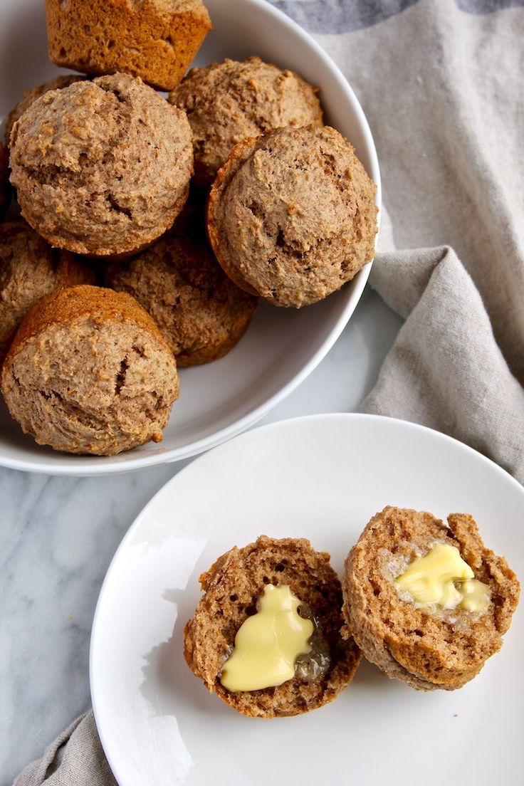 some muffins are on a white plate and next to a bowl of butter