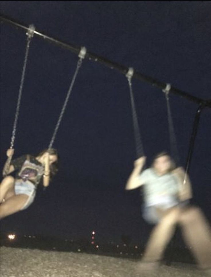 two girls are swinging on swings at night