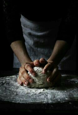 a person kneading dough on top of a wooden table in front of a black background