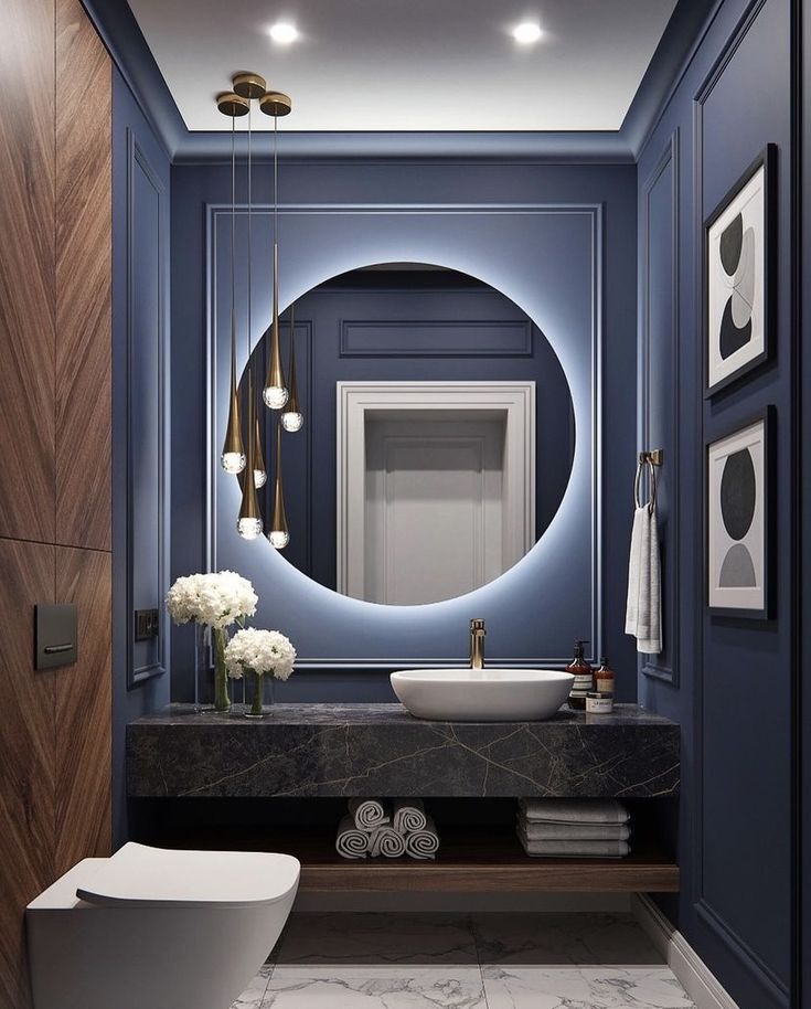 a modern bathroom with blue walls and marble countertop, round mirror above the sink