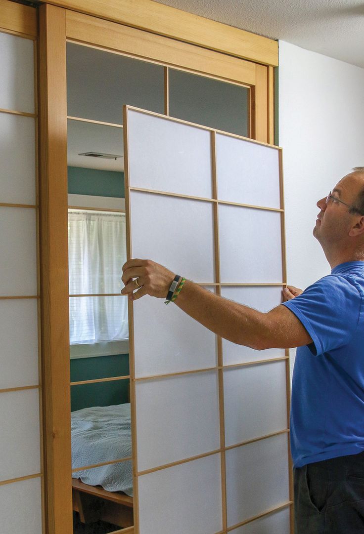 a man in blue shirt and black shorts holding up a white paneled wall next to a bed