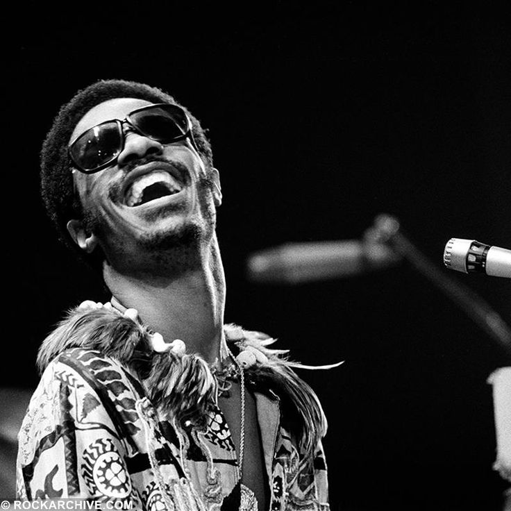 a black and white photo of a man singing into a microphone with sunglasses on his head