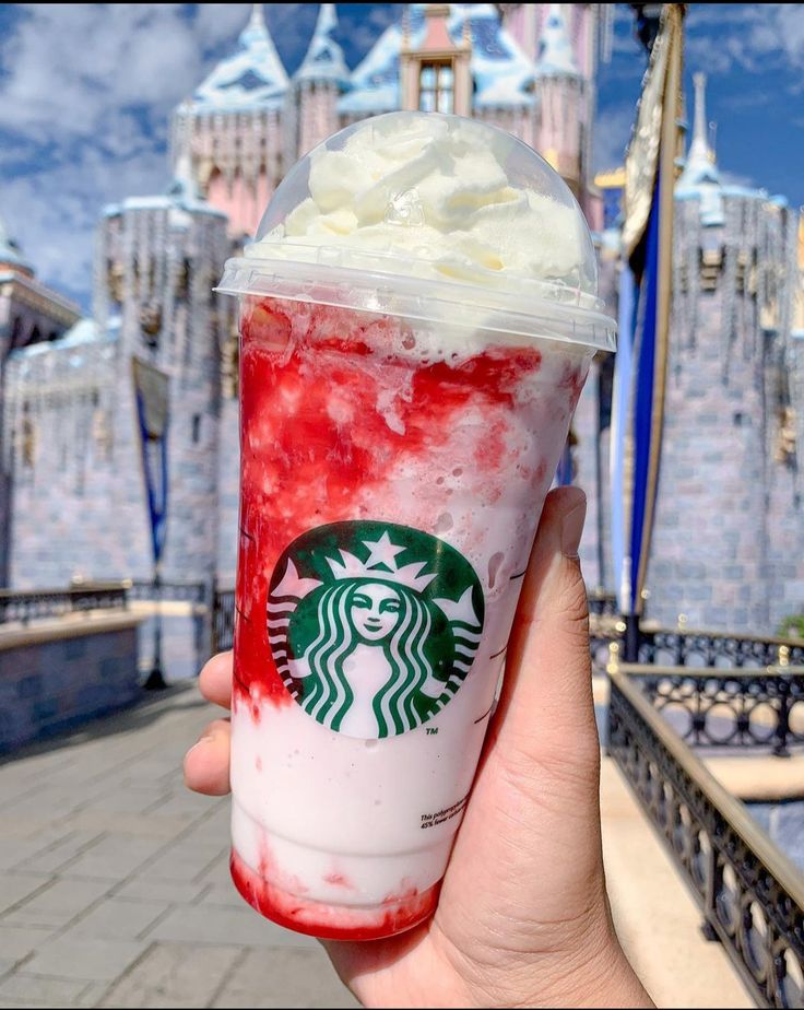 a hand holding up a drink with whipped cream and strawberries on it in front of a castle