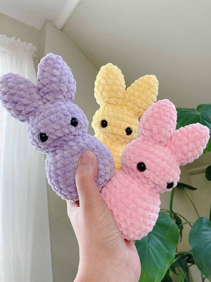 three small crocheted animals are held up in front of a plant