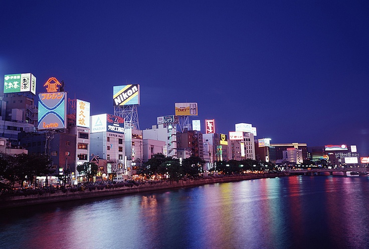 the city is lit up at night and reflecting in the water with its lights on