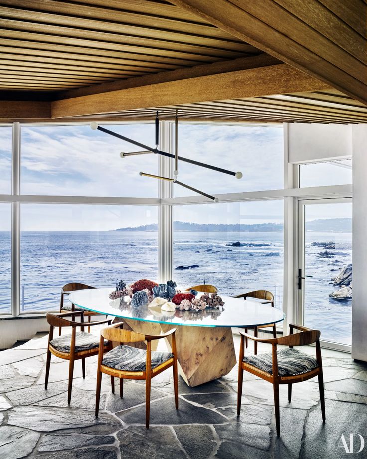 the dining room table is surrounded by wooden chairs and glass windows overlooking the ocean in this modern home