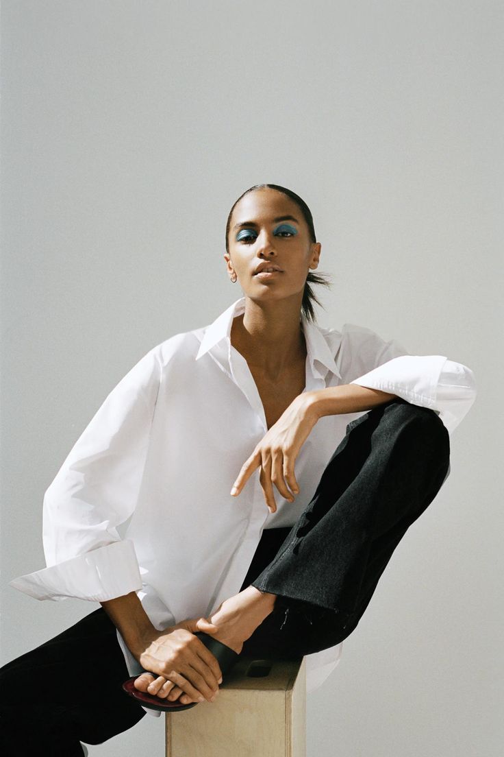 a woman in white shirt and black pants sitting on top of a wooden block with her legs crossed