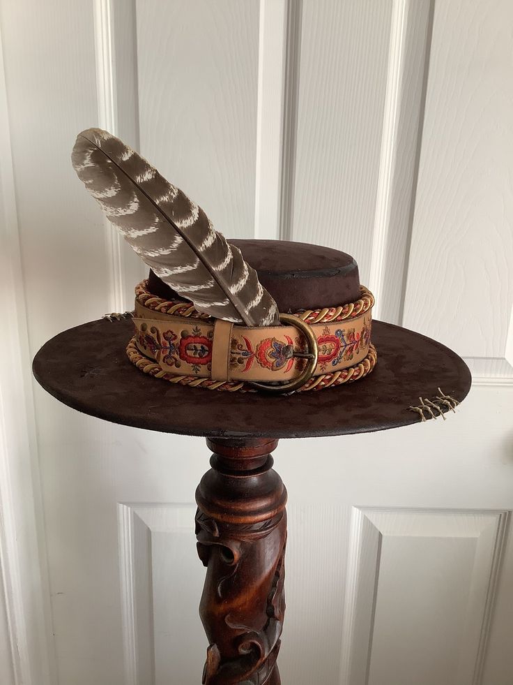 This is a custom weathered hat with incredible detail.  Brown suede hat wIth decorative leather trim and brass bucke.  Topped with feathers, multi colored cording, vintage buttons and tan stitching.  Adjustable band in side. Vintage Top Hat For Western-themed Events, Vintage Handmade Hat Band For Western-themed Events, Vintage Leather Fedora Hat Band, Western Style Brown Mini Hats For Festival, Vintage Handmade Brown Hat Bands, Brown Western Mini Hats For Festivals, Vintage Brown Fedora With High Crown, Vintage Brown Handmade Hat Bands, Vintage Brown Mini Hat With Flat Brim