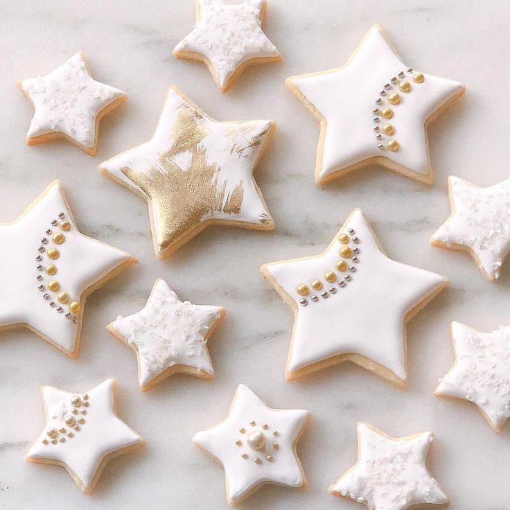 decorated sugar cookies arranged in the shape of stars on a marble countertop with gold and white icing