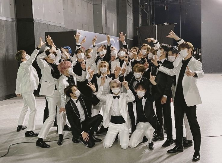 a group of young men in tuxedos posing for a photo with their hands up