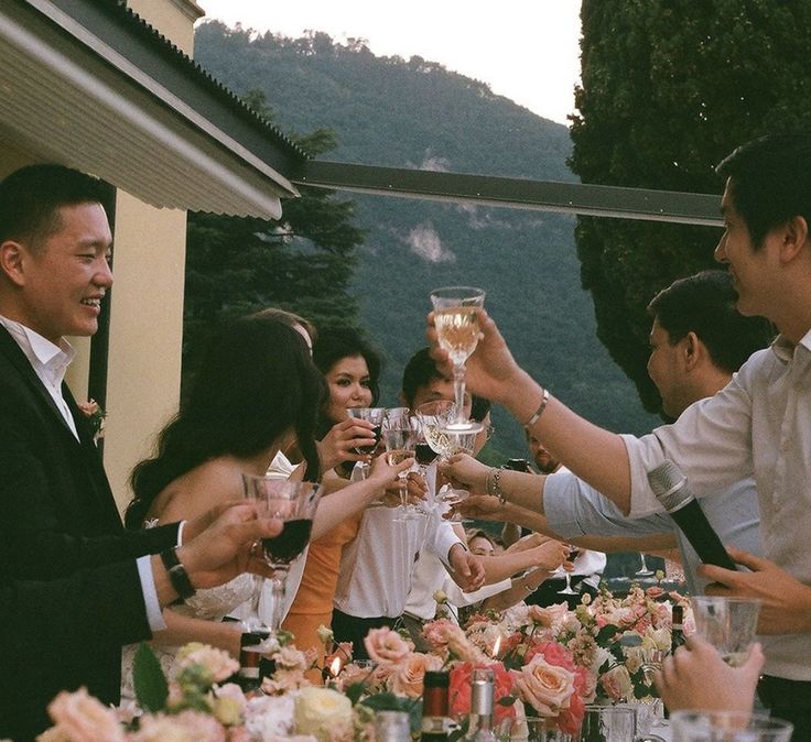 a group of people standing around a table with wine glasses in their hands and flowers on the table