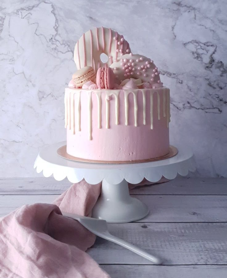 a pink cake sitting on top of a white cake stand next to a pink blanket