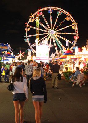 two girls standing in front of a carnival at night with ferris wheel in the background