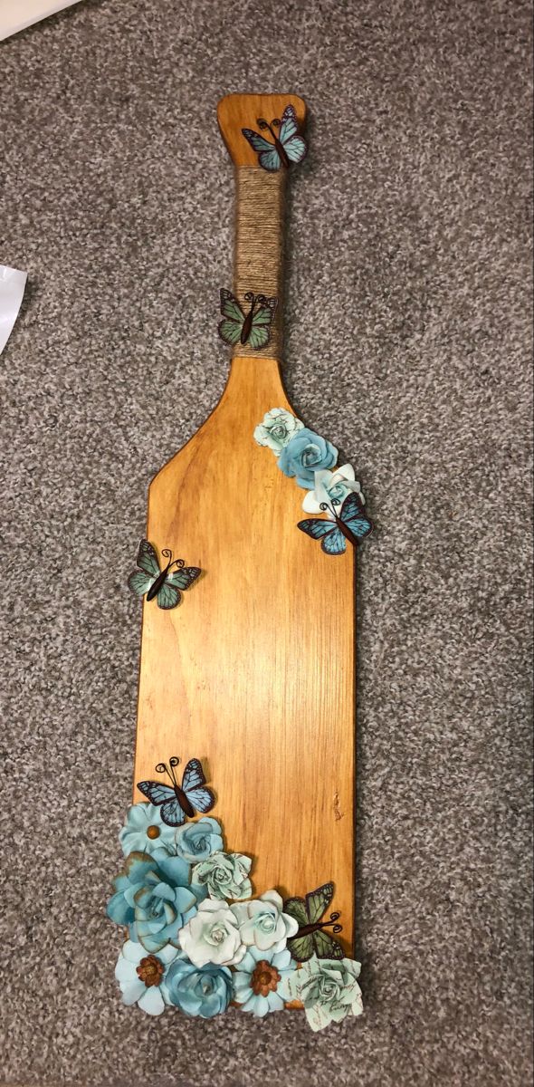 a wooden cutting board with flowers and butterflies on the handle, sitting on carpeted area