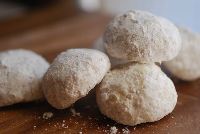 four snowball cookies sitting on top of a wooden table next to other doughnuts