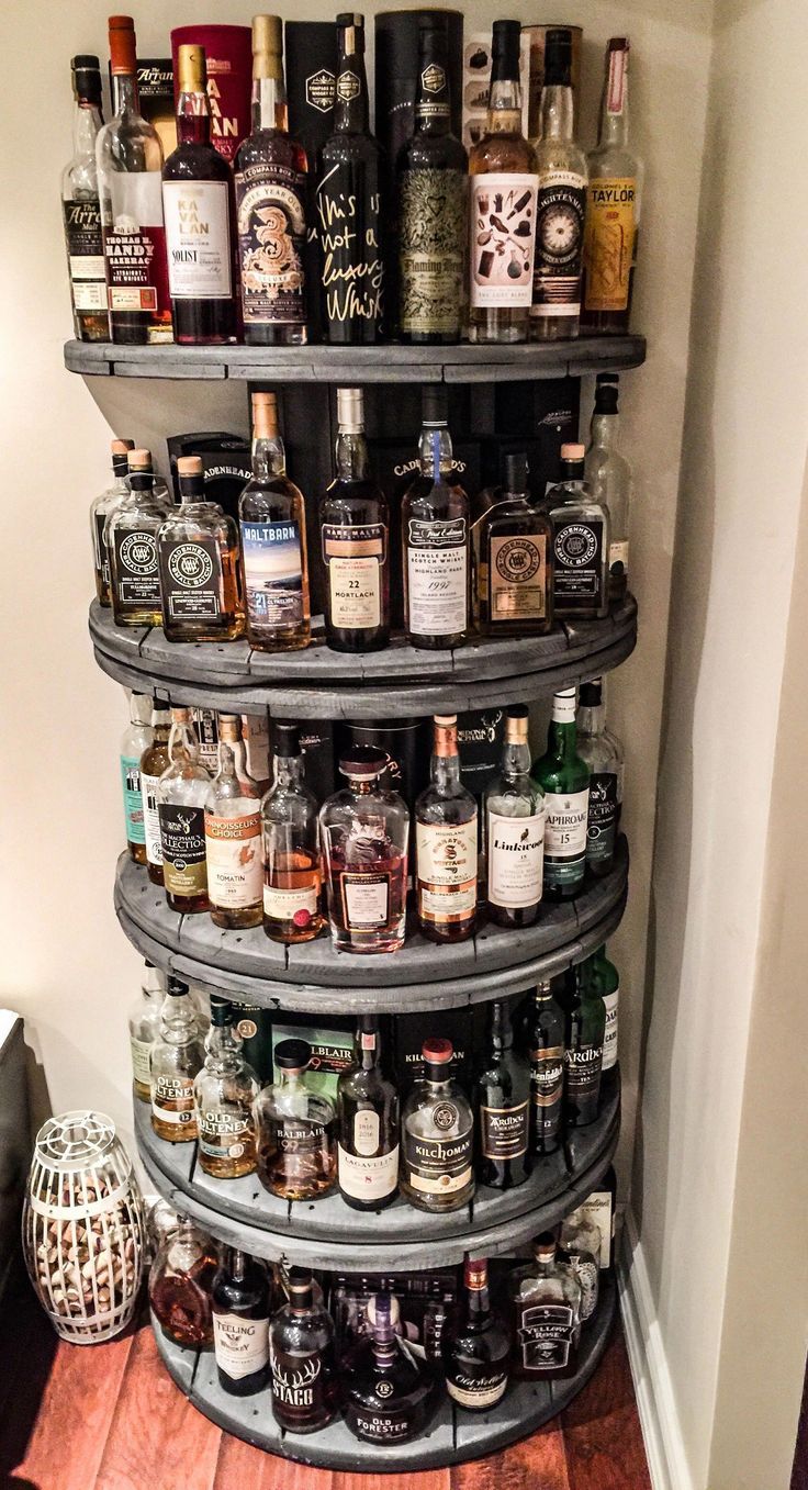 a tall shelf filled with lots of liquor bottles on top of a wooden floor next to a wall