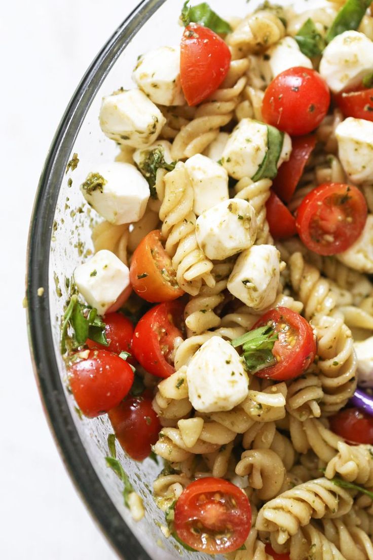 pasta salad with tomatoes, mozzarella and basil in a glass bowl on a white surface