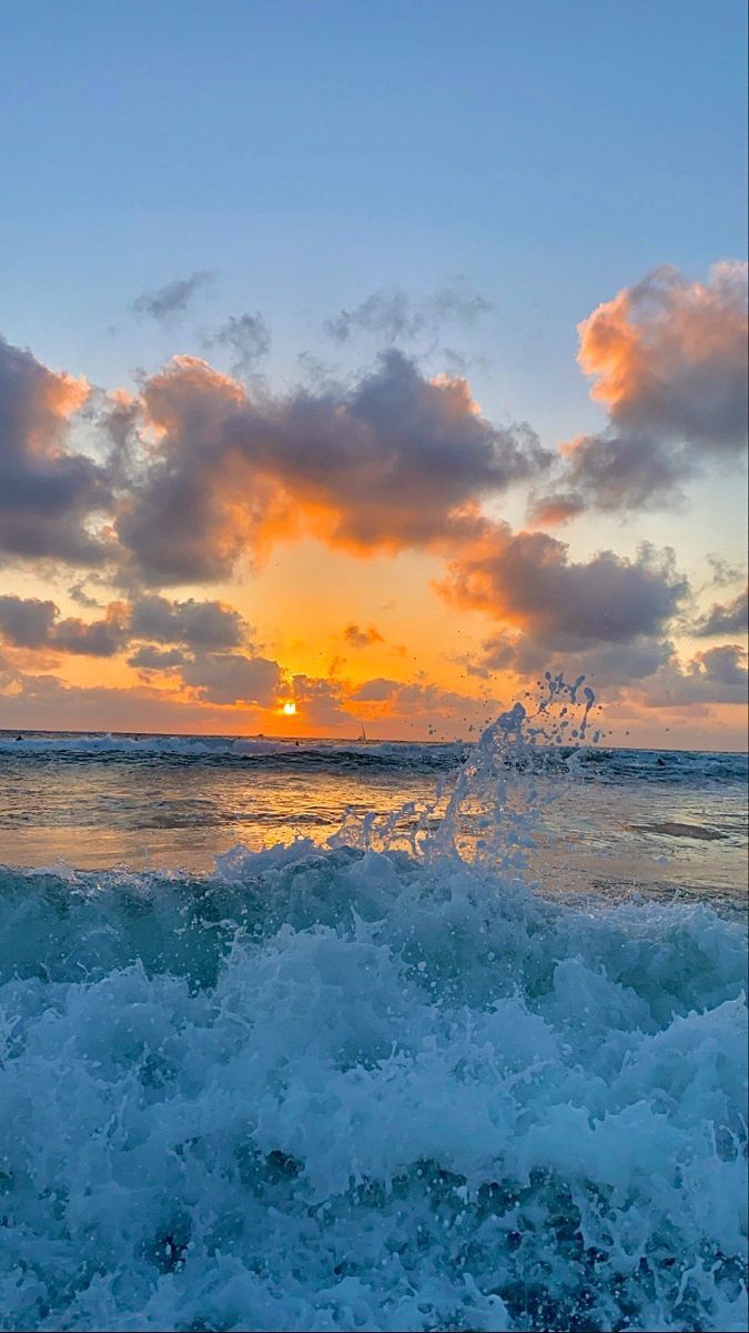 the sun is setting over the ocean with waves crashing in front of it and some clouds