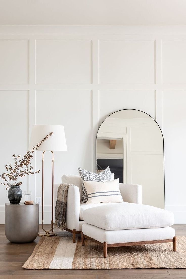 a living room with white walls and wooden flooring, a large mirror on the wall