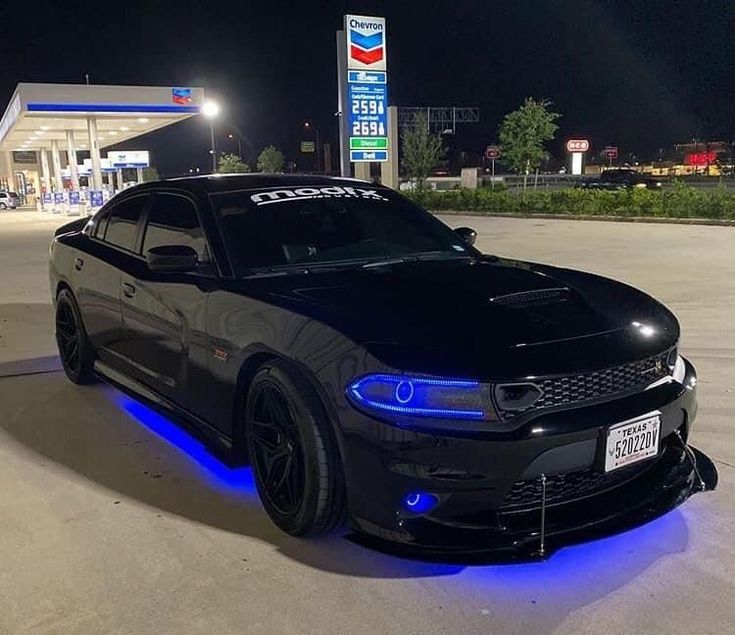 a black car with blue lights on it's hood parked in front of a gas station