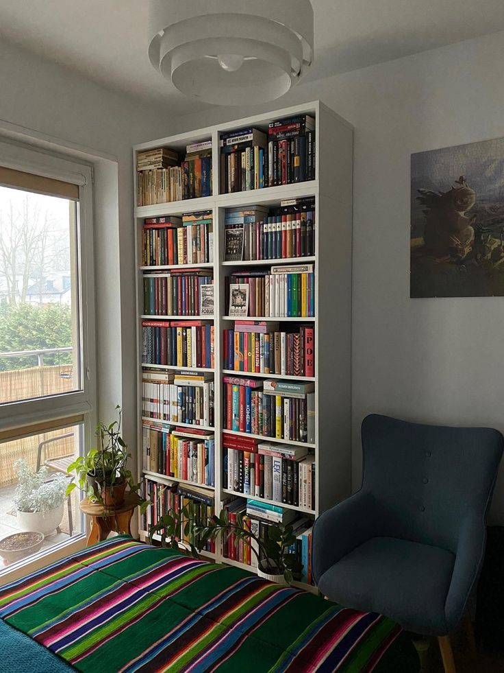 a bedroom with a bed, chair and bookshelf filled with lots of books