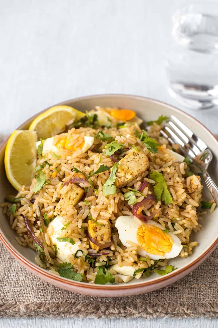 a bowl filled with rice and fried eggs on top of a table next to a glass of water