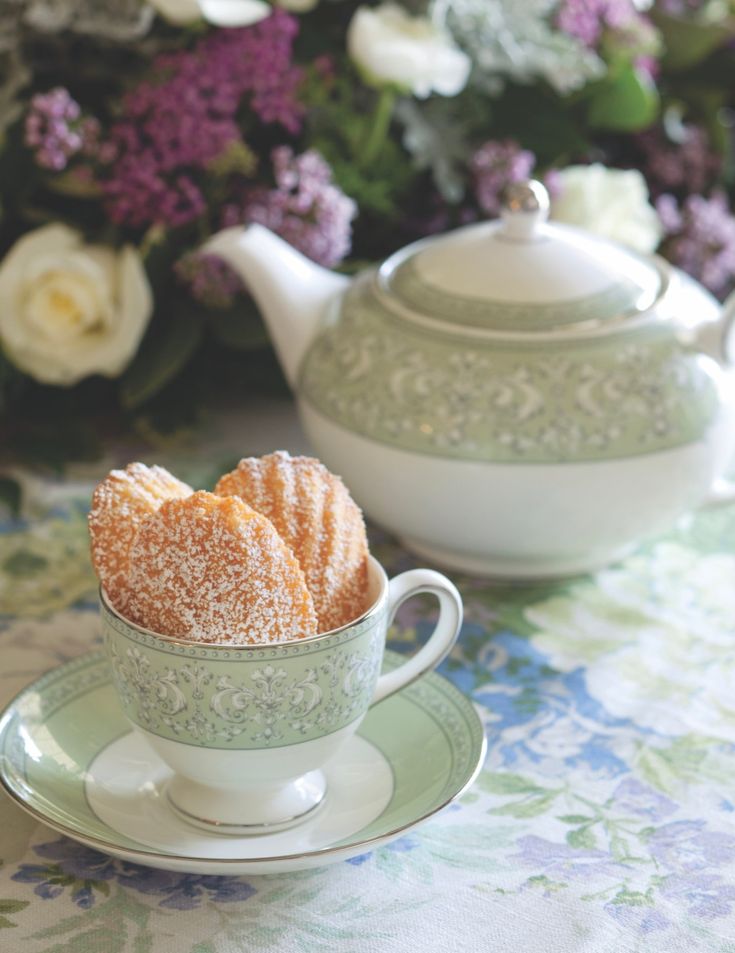 powdered sugar sits in a teacup on a table next to a floral arrangement