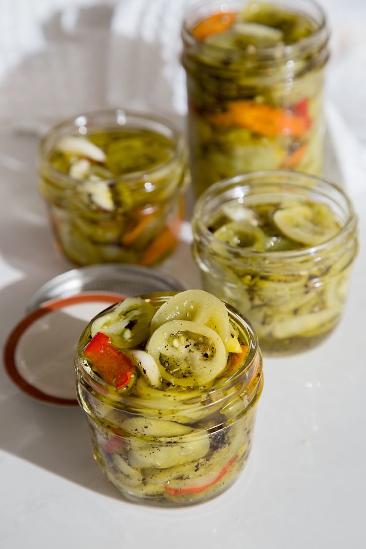 pickles and onions in jars on a white tablecloth with spoons next to them