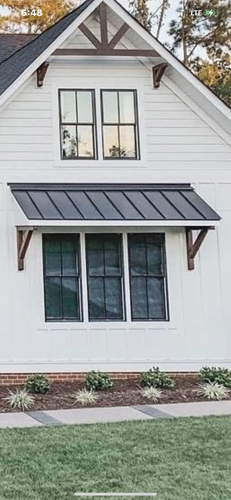 a white house with a black metal roof and two large windows on the second floor