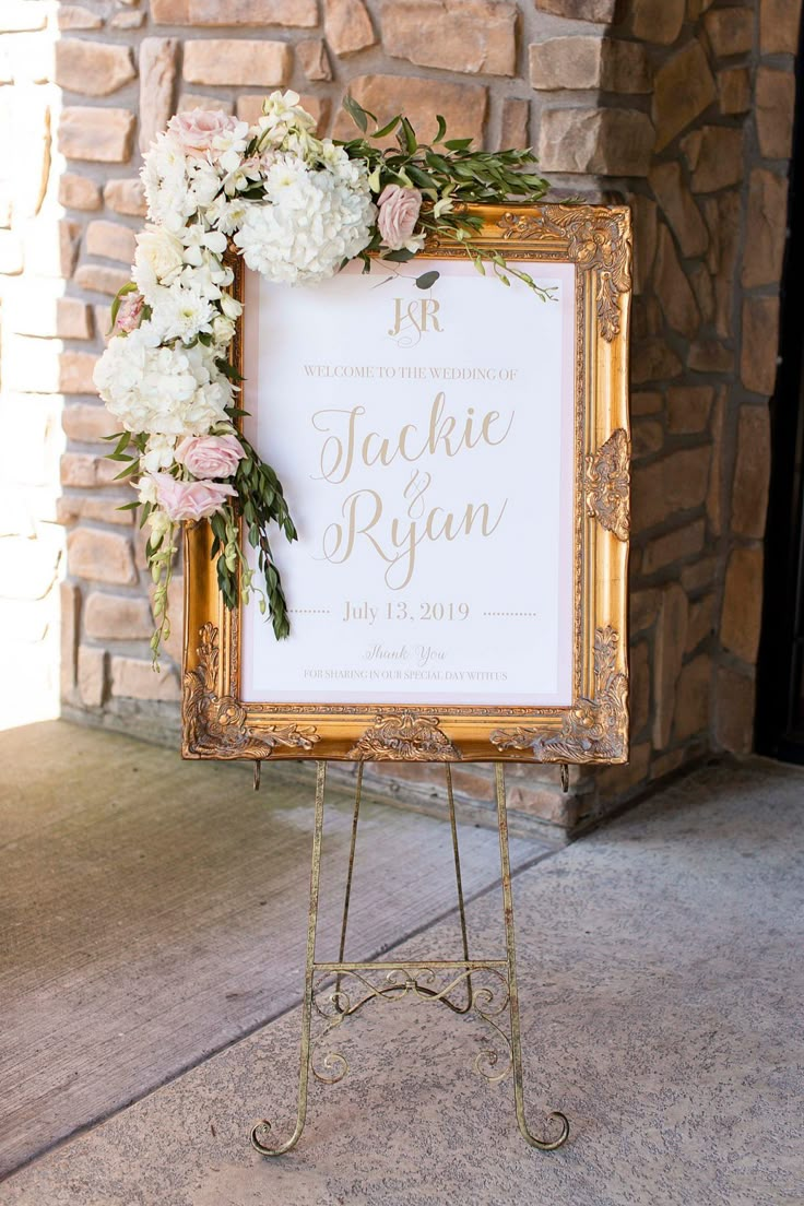 a sign with flowers on it sitting in front of a brick wall