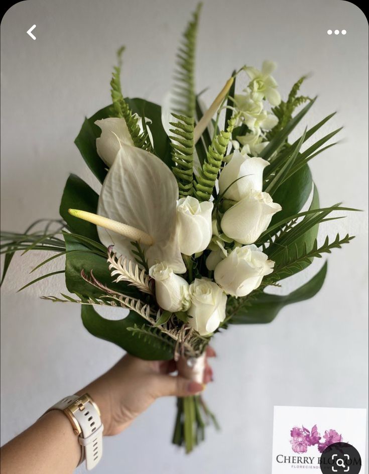 a person holding a bouquet of white flowers and greenery in front of a wall