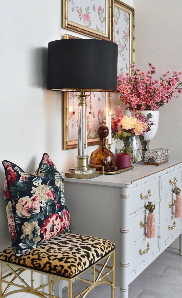 a white dresser topped with a mirror next to a lamp and flowers on top of it