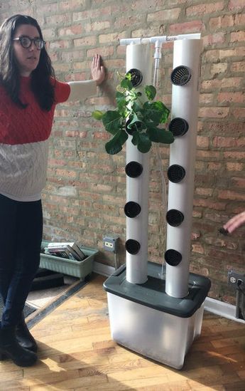 a woman standing next to a tall planter with plants growing out of it's sides