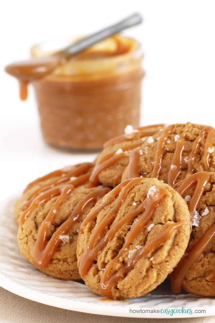 peanut butter cookies with drizzled caramel are on a plate next to a jar of peanut butter