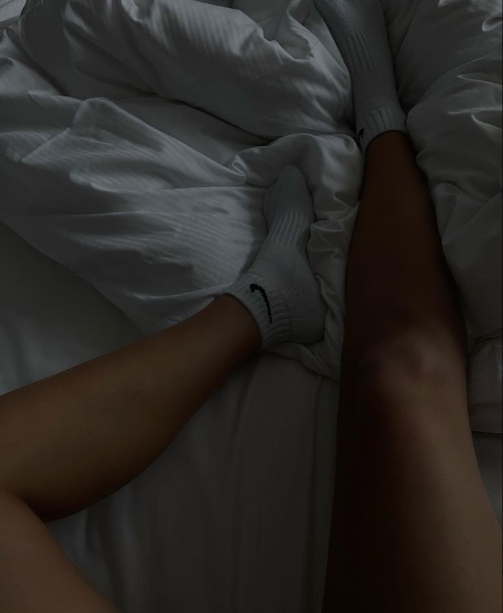 a person laying in bed with white sheets and socks on their feet, under the covers