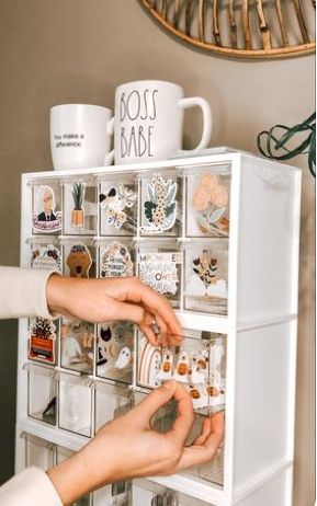 two hands reaching for magnets on top of a white cabinet with drawers and mugs