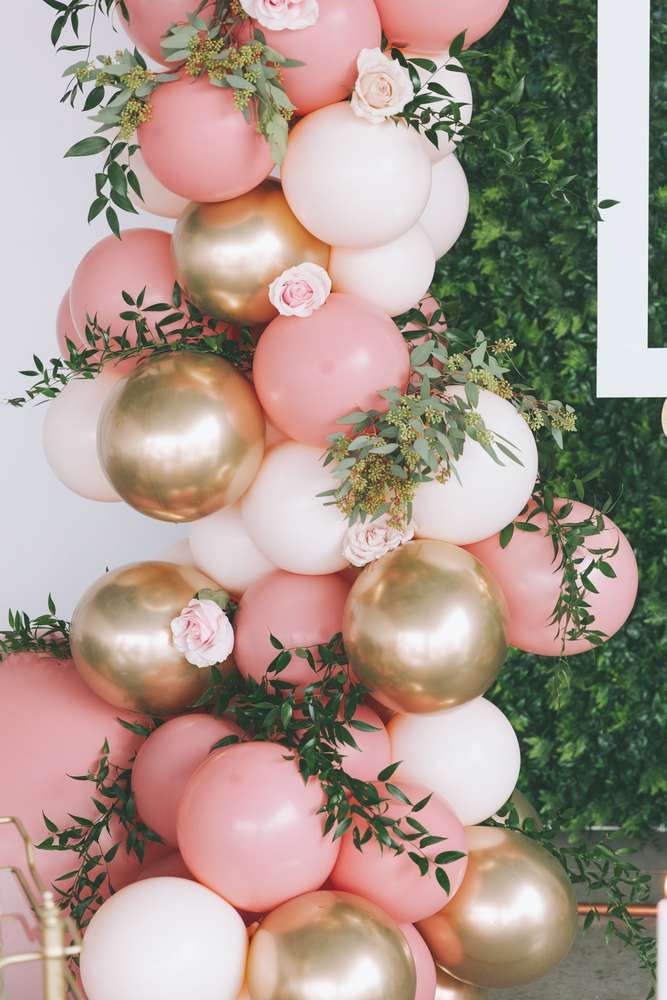 balloons and greenery are arranged on the wall for a balloon arch with pink, white and gold balloons