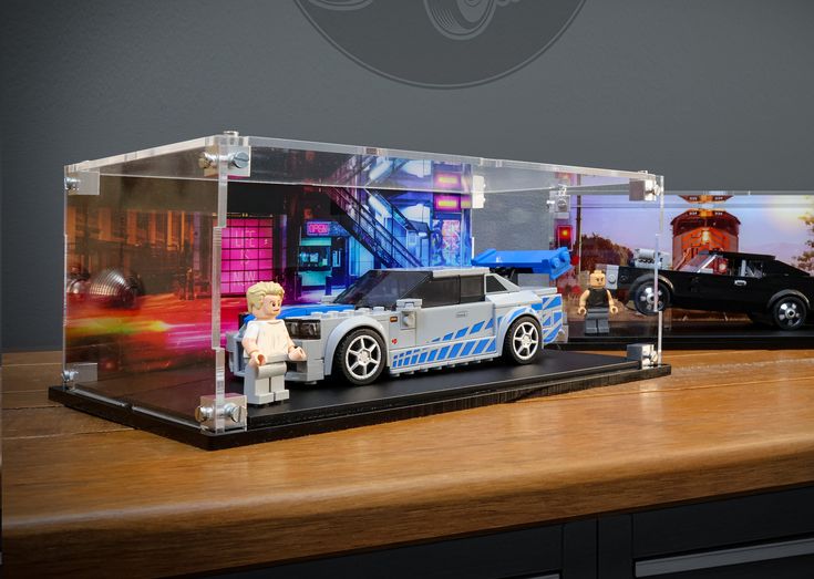 two legos are sitting in front of a display case with cars on the table