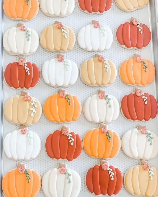 decorated pumpkin cookies are arranged in rows on a baking sheet, ready to be eaten