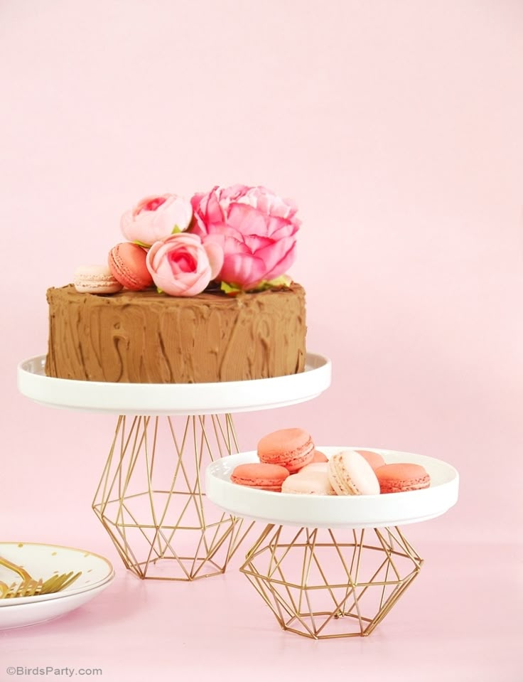 three tiered cake stands with macaroons and flowers on top, against a pink background