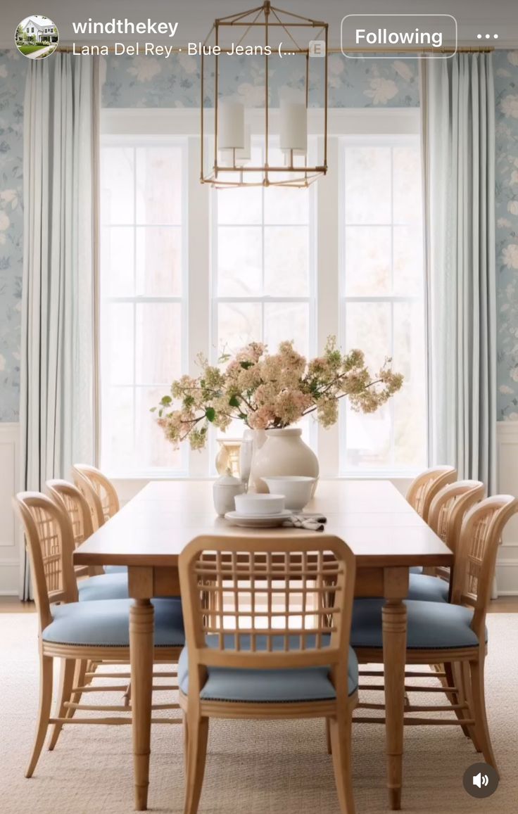 a dining room table with blue chairs and flowers in a vase on the centerpiece