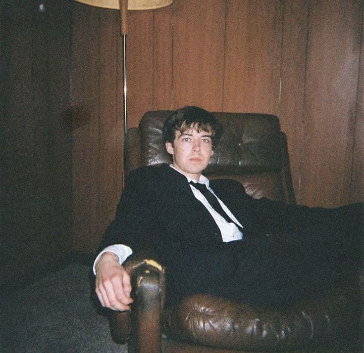 a man in a suit and tie sitting in a chair with his feet up on the floor