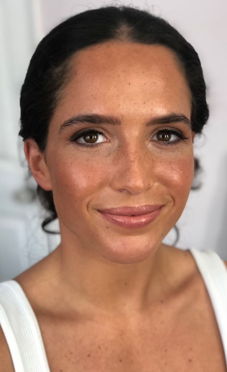 a woman with freckled hair smiling at the camera and wearing a white tank top