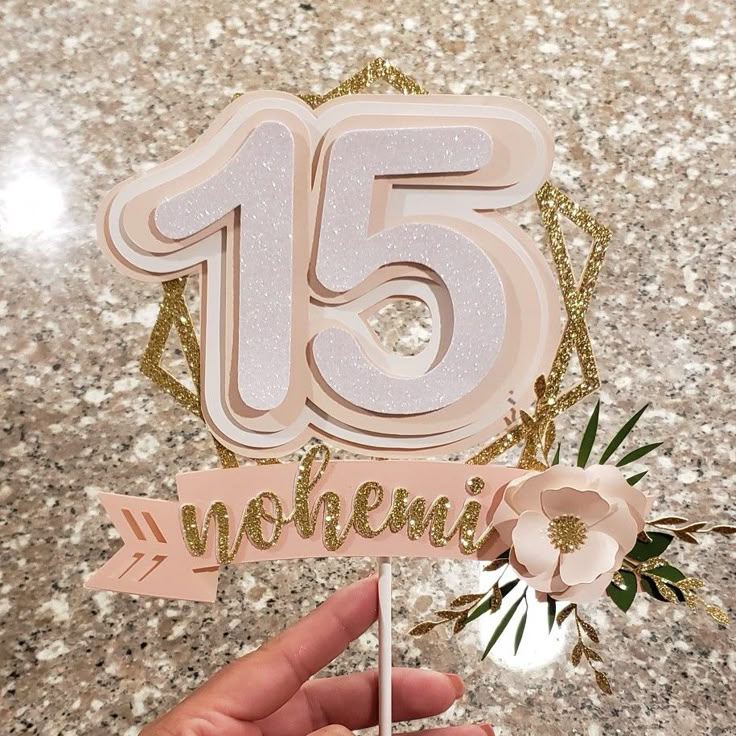 someone is holding up a cake topper with the number fifteen on it and flowers