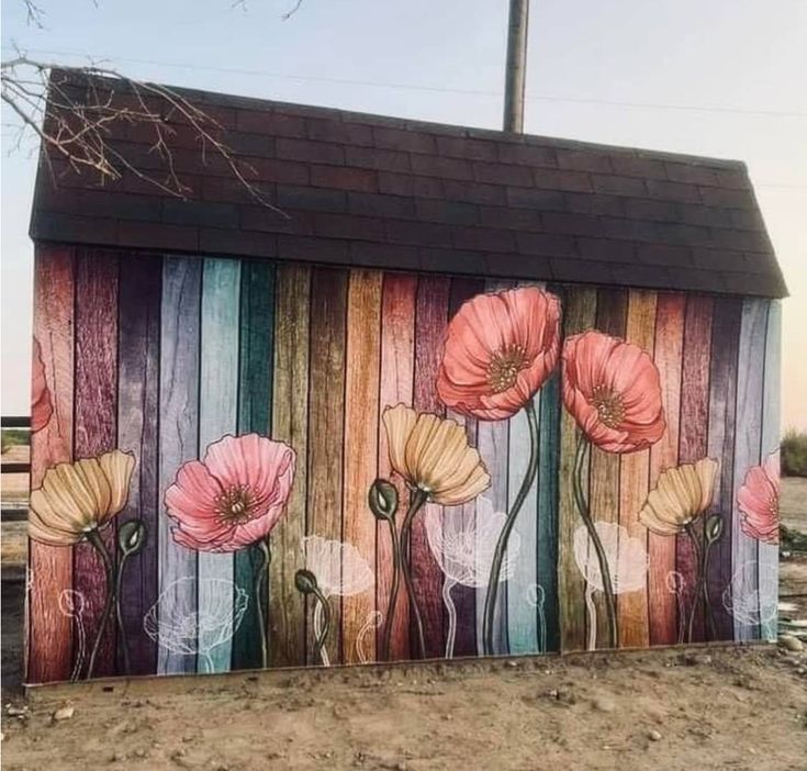 a painted wall with flowers on it and a wooden fence in the foreground, next to a building