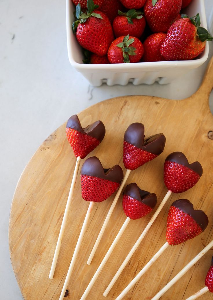 chocolate covered strawberries are arranged on sticks in front of a bowl of strawberries